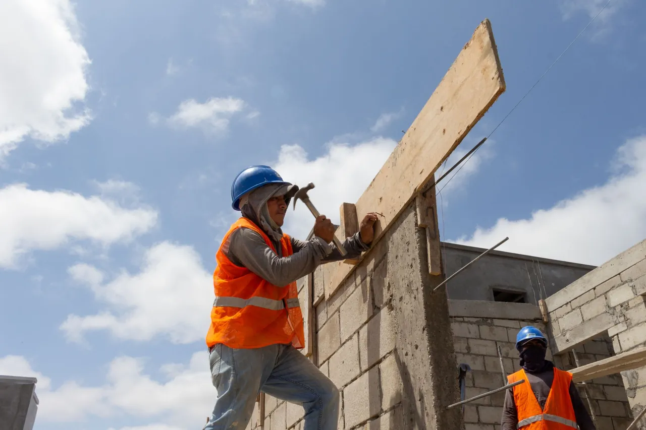 A construction worker in a hard hat and safety vest nailing formwork on a block wall