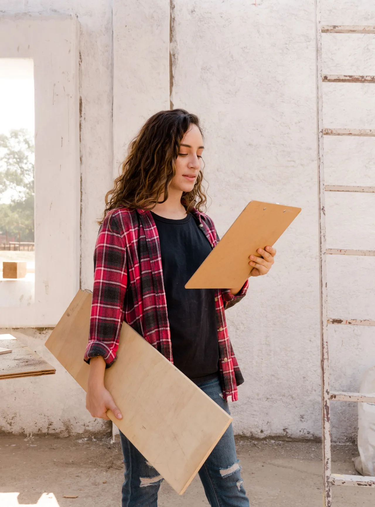 A woman with a clipboard and a sheet of plywood checking her list at a construction site